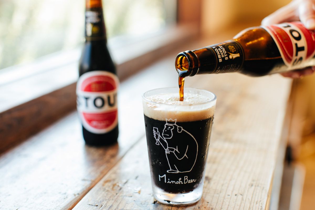 A dark beer pouring from a bottle into a glass.